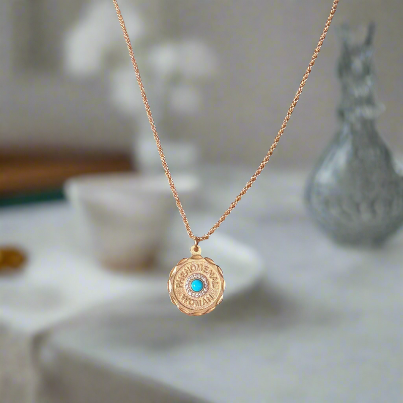 Gold necklace with a blue pendant on a person wearing a dark top.